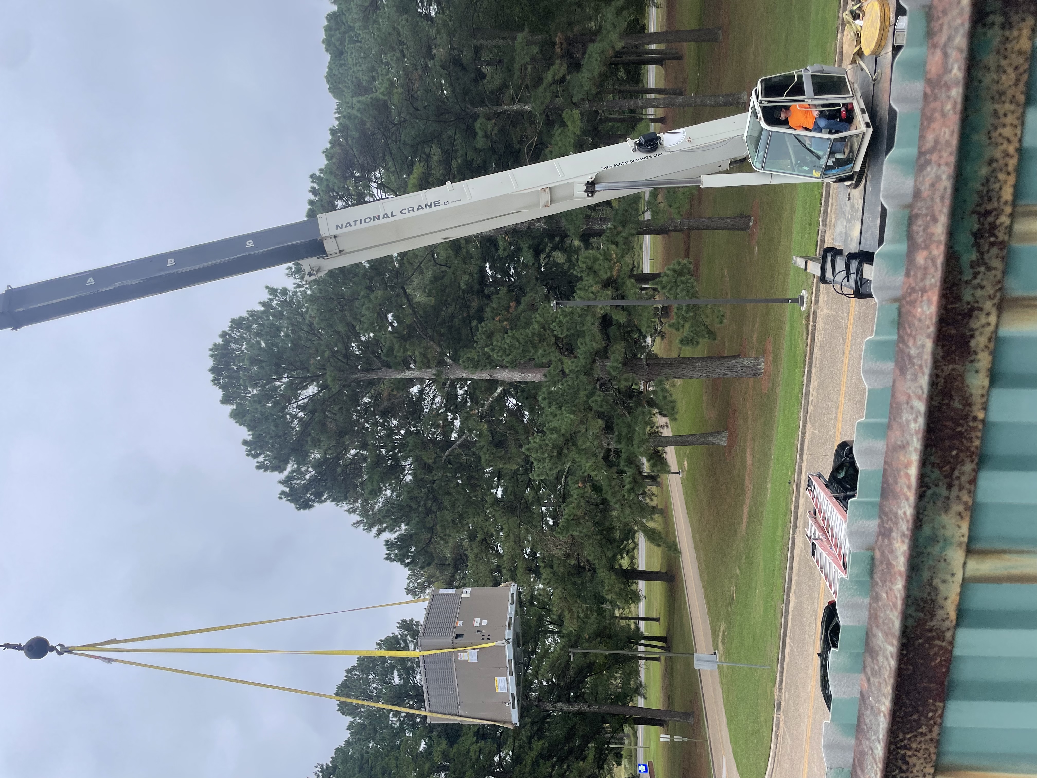 A packaged rooftop HVAC unit hoisted in the air by a crane during a commercial installation