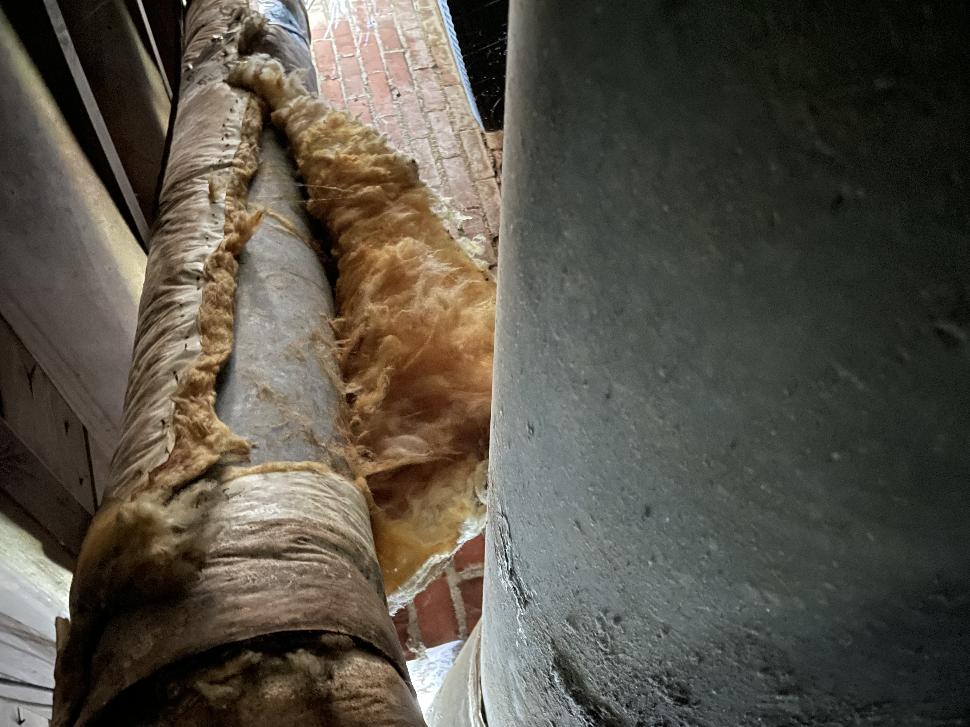 HVAC duct with its insulation torn open, exposing bare metal where conditioned air leaks