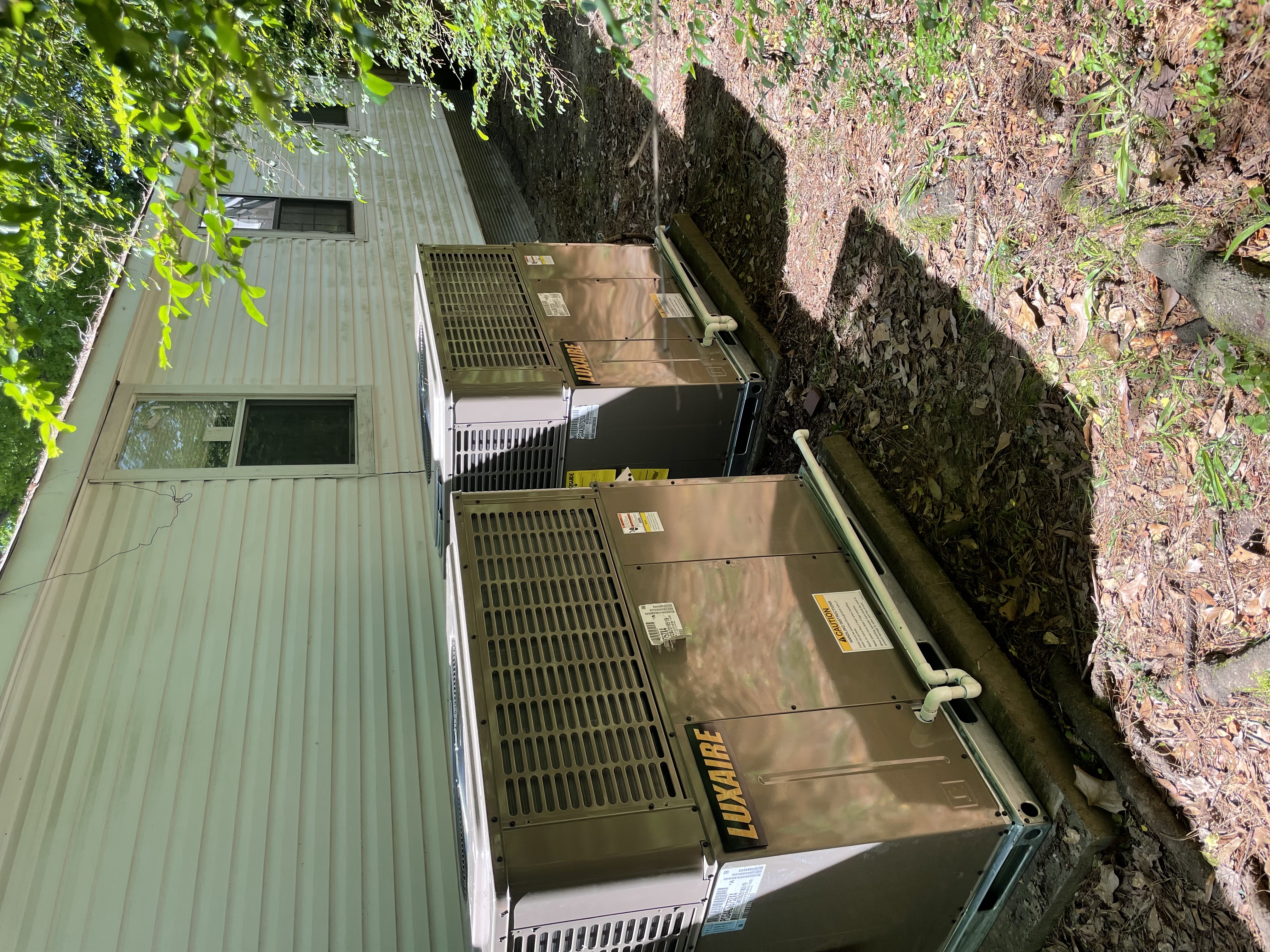 Two new Luxaire packaged HVAC units installed on pads beside a manufactured home